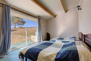 A bedroom with two beds, a large window, and a view of a tree and landscape.