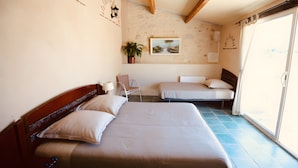 A room with two beds, a chair, a potted plant, a painting, and a window with curtains.