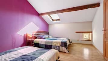 A bedroom with two beds, a skylight, wooden beams, and a small window.