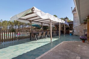 A covered outdoor seating area with a pool in the background.