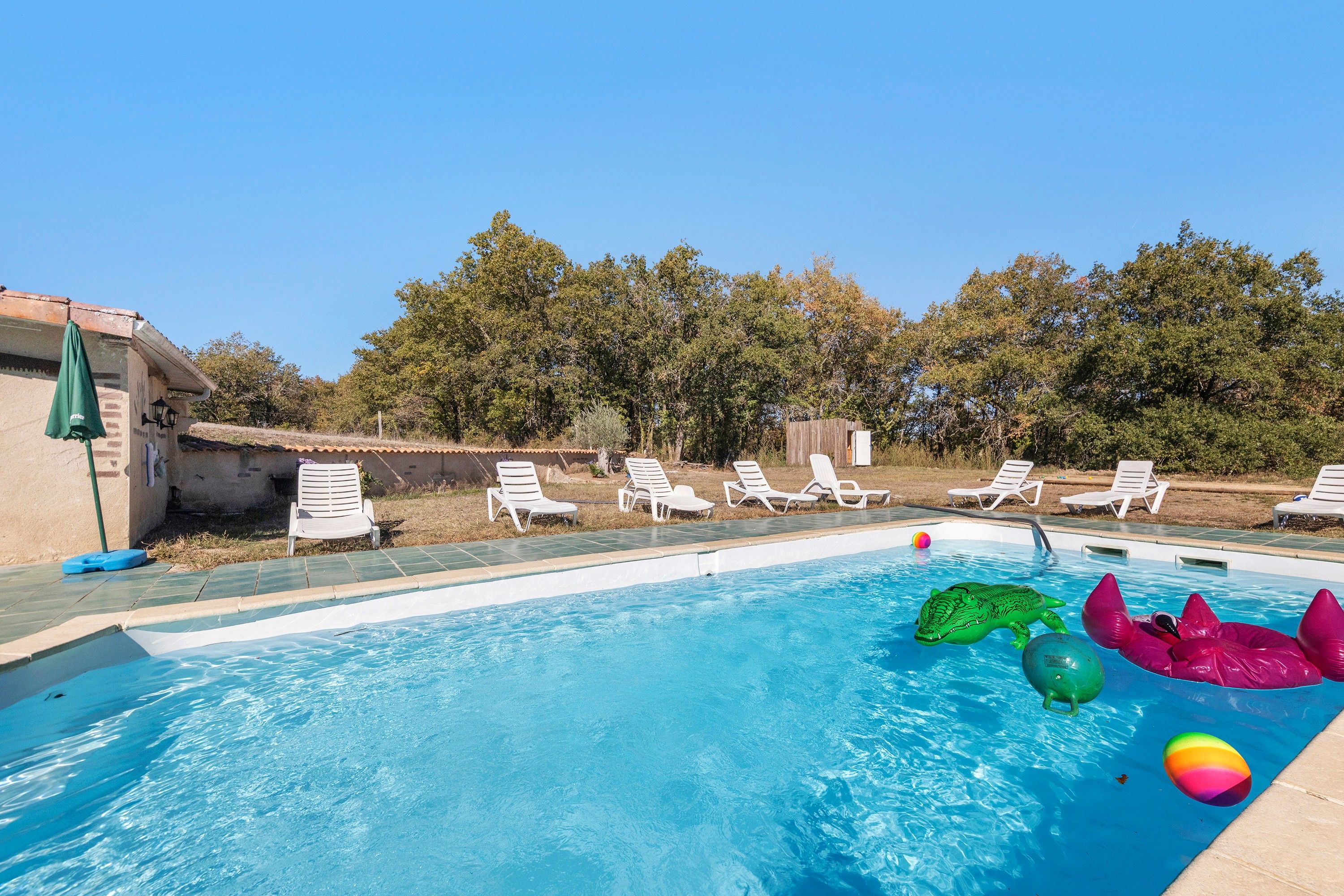 Una piscina con agua azul cristalina, rodeada de sillones blancos y una terraza de madera.