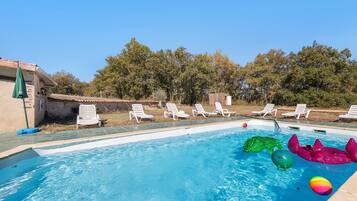 Una piscina con agua azul cristalina, rodeada de sillones blancos y una terraza de madera.