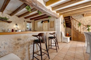 A rustic interior with exposed wooden beams, a stone wall bar area, and a staircase. - Country house 'Seul Au Monde' with private pool, terrace and private garden (Guizengeard)