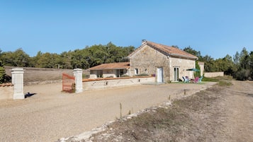 A stone building with a tiled roof, a gravel driveway, and a fenced area with a gate.