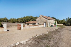 A stone building with a tiled roof, a gravel driveway, and a fenced area with a gate. - Country house 'Seul Au Monde' with private pool, terrace and private garden (Guizengeard)
