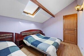 A bedroom with two beds, a skylight, a wooden door, and a wall-mounted light fixture.