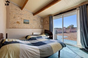 A bedroom with two beds, a stone wall, a painting, and a view through a large window.