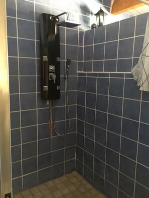 A shower with a handheld showerhead and a wall-mounted faucet, tiled in a grid pattern.