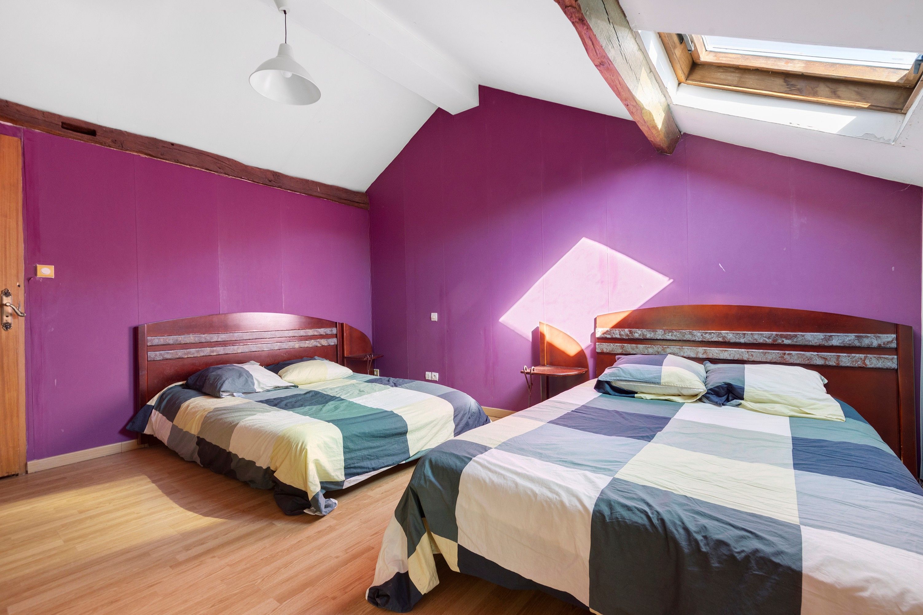A bedroom with two beds, wooden headboards, a skylight, and purple walls.