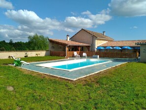 Une maison avec une piscine, une terrasse en bois et un patio couvert.
