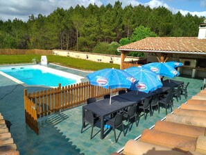 A pool area with a wooden fence, a table with chairs, and blue umbrellas.