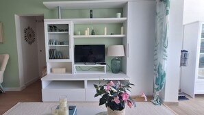 Een woonkamer met een televisie, planken, een stoel en een plant.