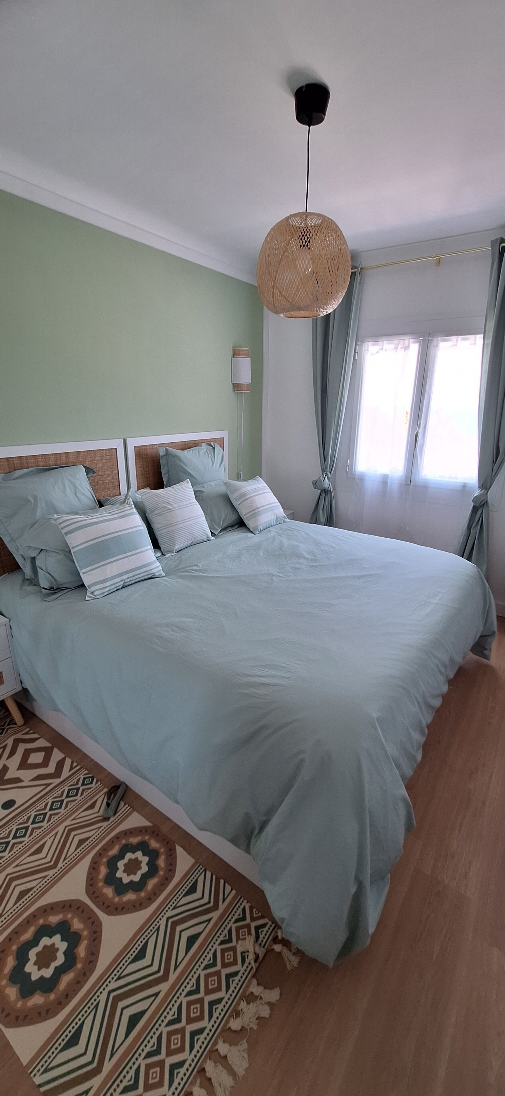 A bed with a light blue bedspread, a woven headboard, and a bedside table with a lamp.