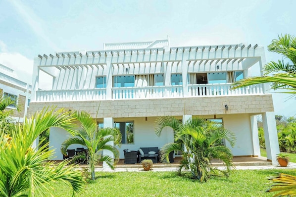 A two-story building with a balcony, a covered outdoor seating area, and a well-maintained garden with palm trees.