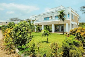 A modern two-story building with a flat roof, large windows, and a well-maintained garden with various plants and a palm tree.