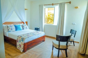 A bedroom with a wooden bed, a chair, a window with curtains, and a view of palm trees outside. - Luxurious 5-bedroom Villa With Private Pool in Diani, Kenya (Diani Beach)