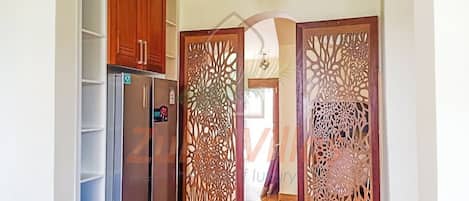 A kitchen with a refrigerator, wooden cabinets, and a decorative partition.