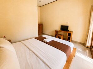 A hotel room with a bed, a wooden desk with a television, and a small cabinet.