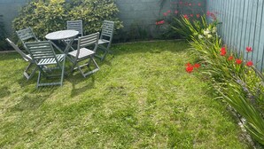 A patio with a round table and chairs, surrounded by a grassy area and a low wall. - Charming Coastal Retrest (Dunmore East)