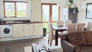 A modern kitchen with a washing machine, a dining area with a table and chairs, and a leather sofa. - Charming Coastal Retrest (Dunmore East)