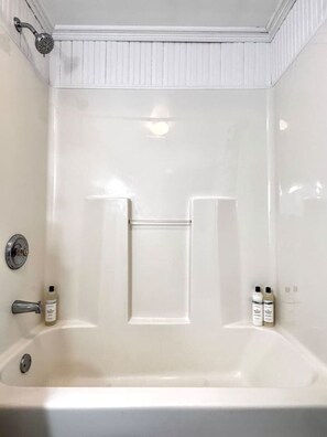 Una bañera blanca con alcachofa de ducha, barra para toallas y dos botellas de champú.