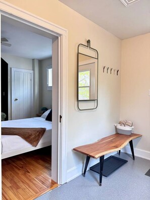 Una habitación con una cama, un banco de madera, un espejo y una cesta en la pared.