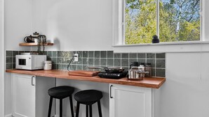 Uma cozinha com bancada de madeira, dois banquetes pretos, micro-ondas branco e janela com vista para árvores.