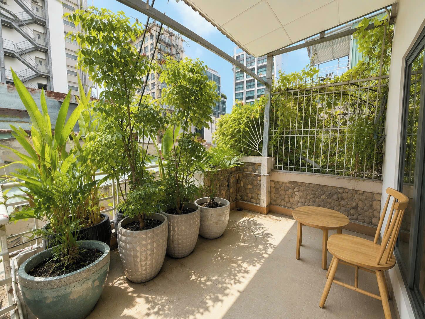 Een balkon met plantenbakken, een houten stoel en uitzicht op gebouwen.