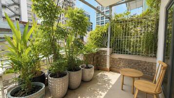 Een balkon met plantenbakken, een houten stoel en uitzicht op gebouwen.