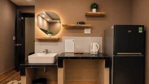 A modern kitchen with a black refrigerator, white sink, and wooden flooring. - Ben Thanh Hideaway - A Cozi Stay  (Ho Chi Minh City)
