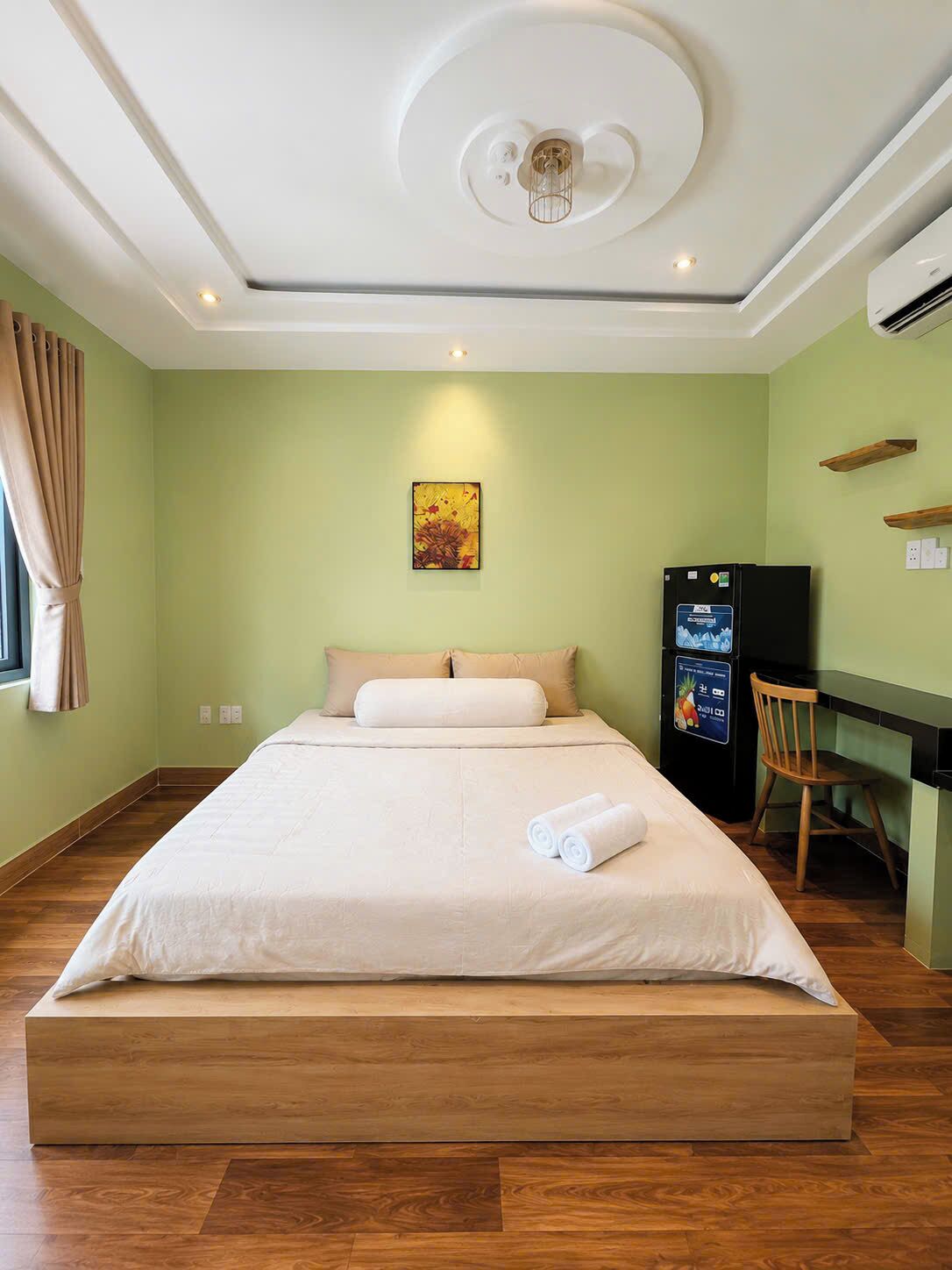 A hotel room with a bed, a desk, a chair, a refrigerator, and a wall-mounted artwork.