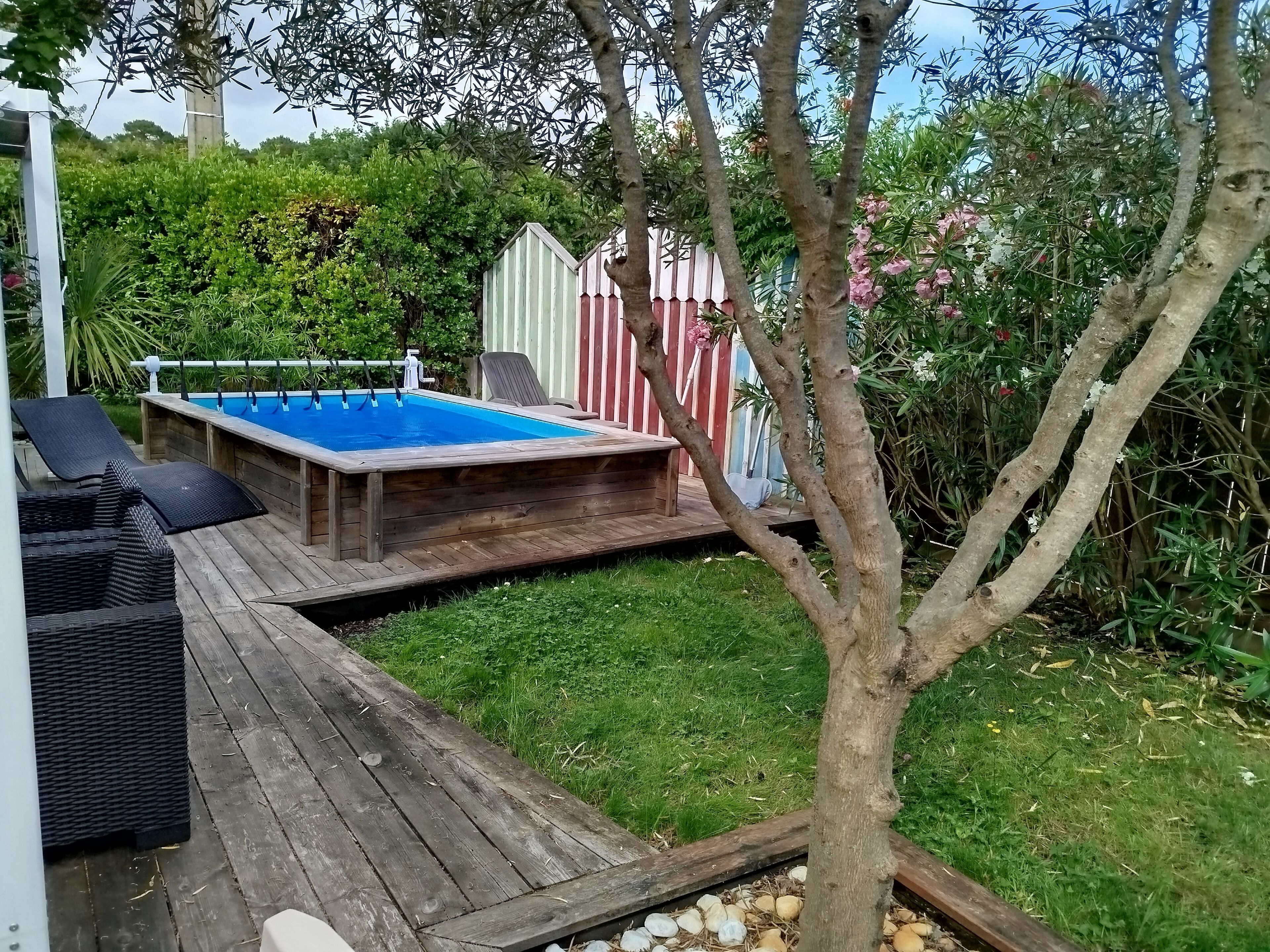 A wooden deck with a swimming pool, lounge chairs, and a small table.