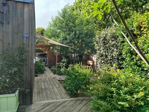 Eine Holzterrasse führt zu einem überdachten Bereich, auf dem ein Schild '17 BIS' zeigt.