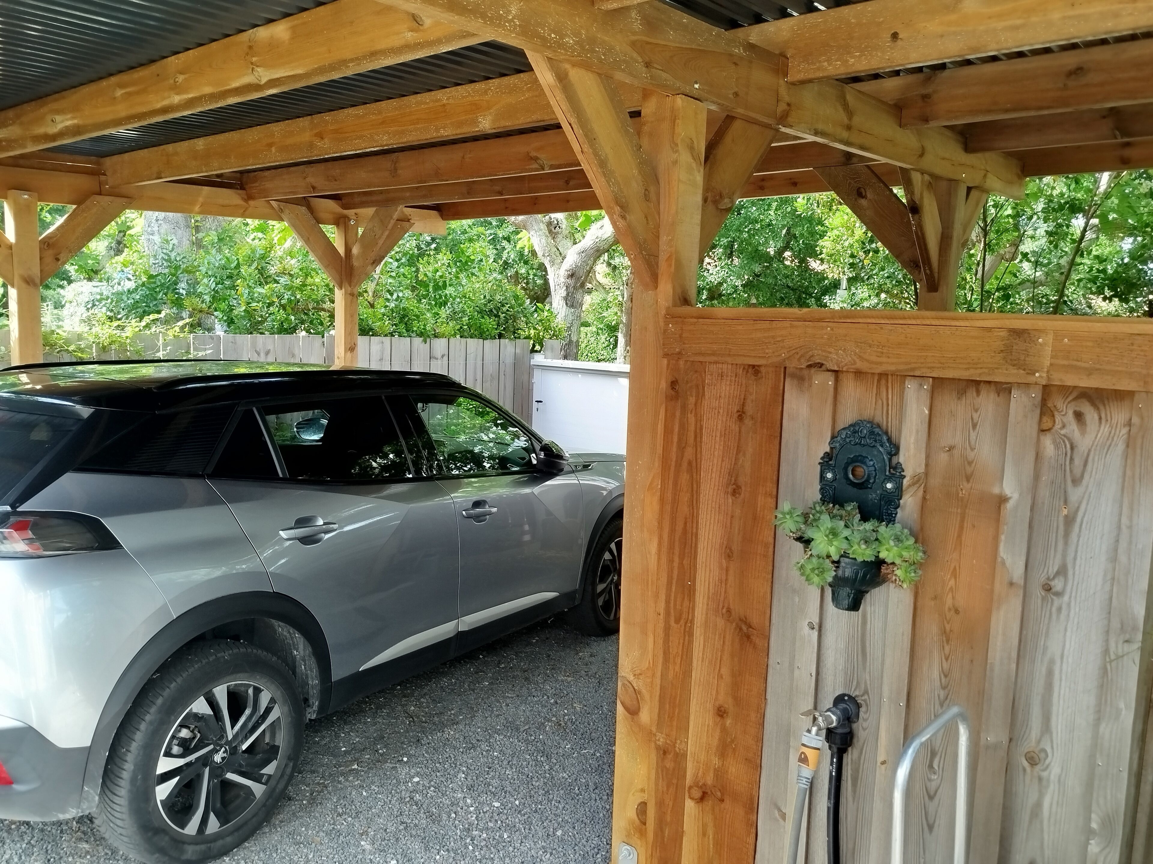 A covered parking area with a car parked under a wooden structure.