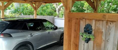A covered parking area with a car parked under a wooden structure.