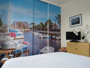 Ein Schlafzimmer mit großem Fenster, einem Bett, einem Fernseher, einer Holzkabine und einem Sessel.
