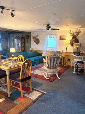 Un salon chaleureux avec une table à manger, des chaises, un fauteuil à bascule, une cheminée et des bois de cerf accrochés au mur.
