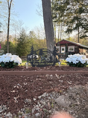 A wooden cabin with a red roof, surrounded by trees and white flowers.