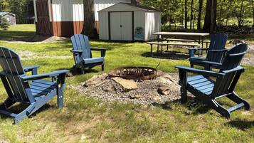 Un terrain de camping équipé de quatre chaises Adirondack, d’un foyer, d’une table de pique-nique et de deux abris de jardin.