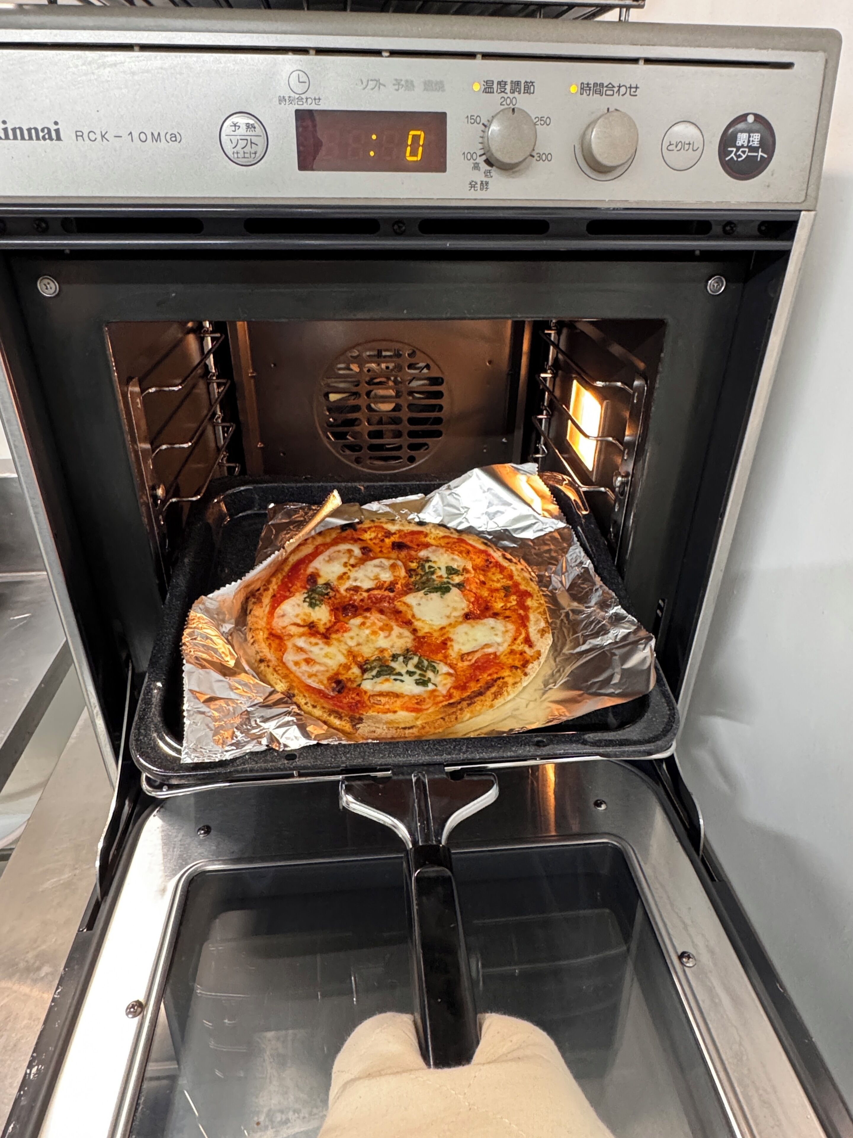 An oven with a pizza inside, a digital display, and control knobs.