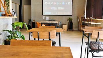 A modern conference room with wooden tables and chairs, a projector screen, and a potted plant.