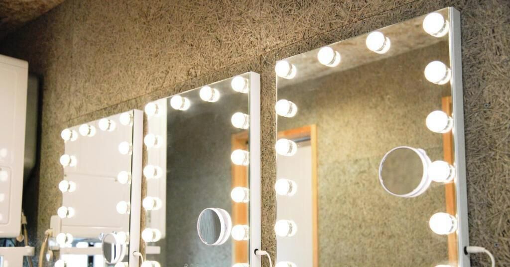 A bathroom with three mirrors surrounded by lights.