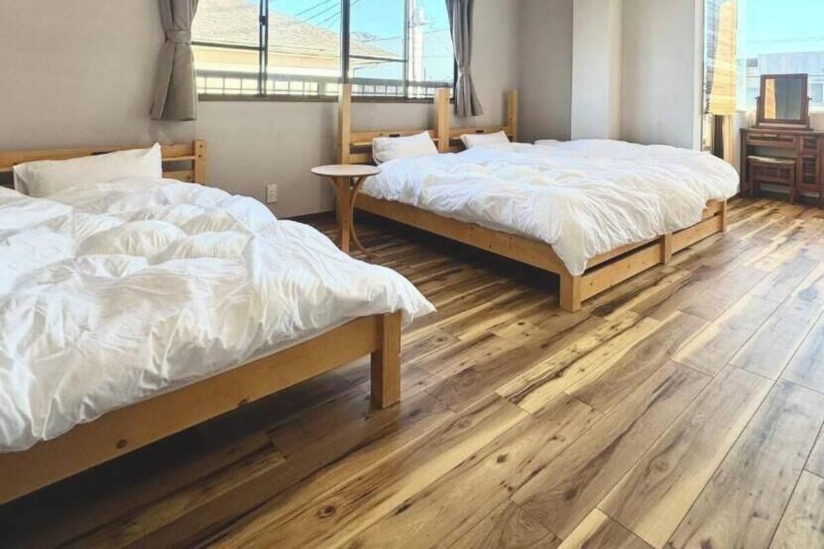 Una habitación con dos camas de madera, una mesita redonda pequeña y un ventanal con cortinas.