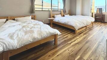 Una habitación con dos camas de madera, una mesita redonda pequeña y un ventanal con cortinas.
