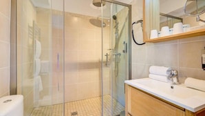 Un baño moderno con ducha envuelta en vidrio, lavamanos blanco y tocador de madera.