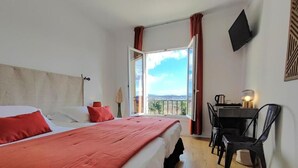 Un dormitorio con cama, escritorio, silla, televisor y ventana con cortinas.