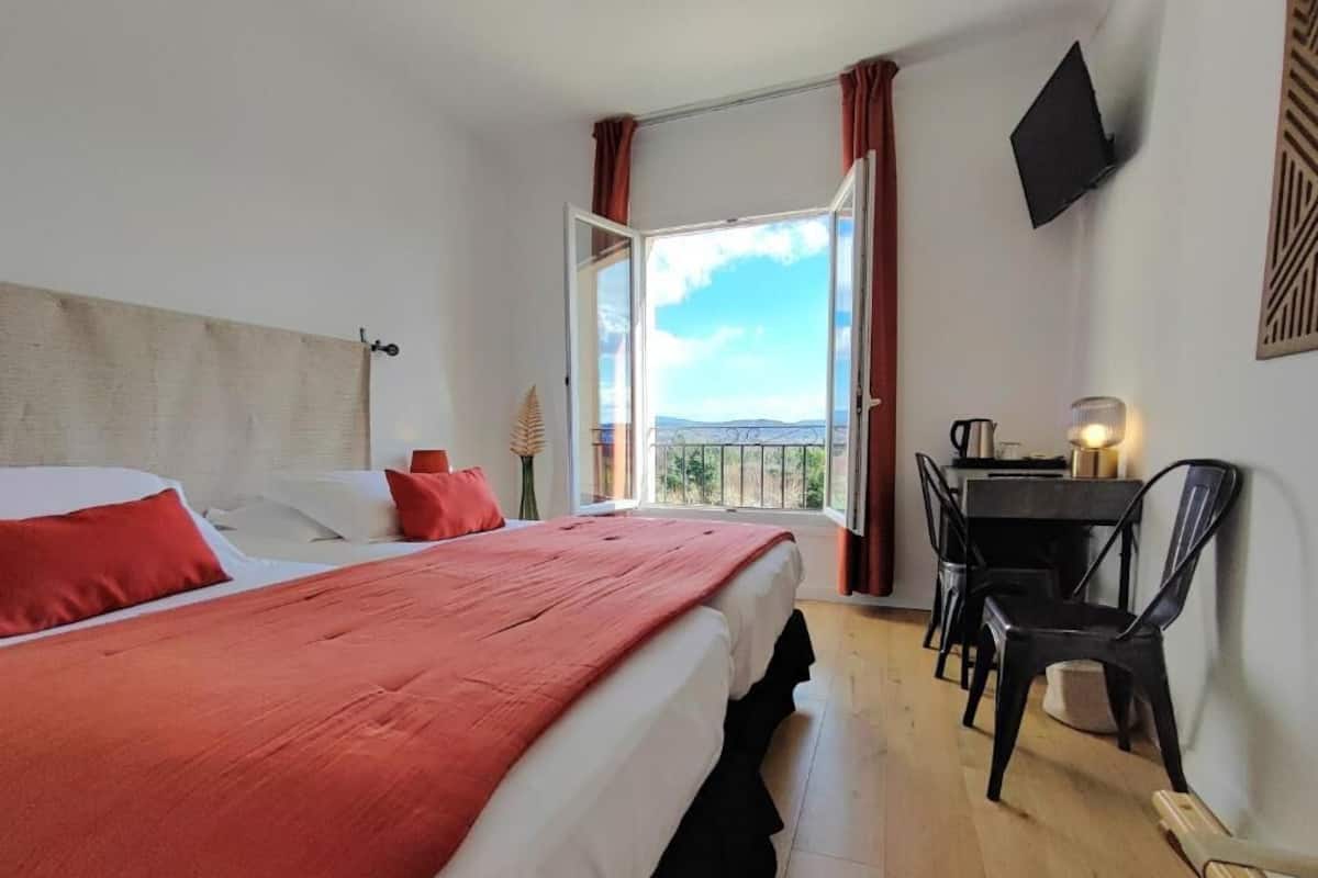 A bedroom with a bed, a desk, a chair, a TV, and a window with curtains.
