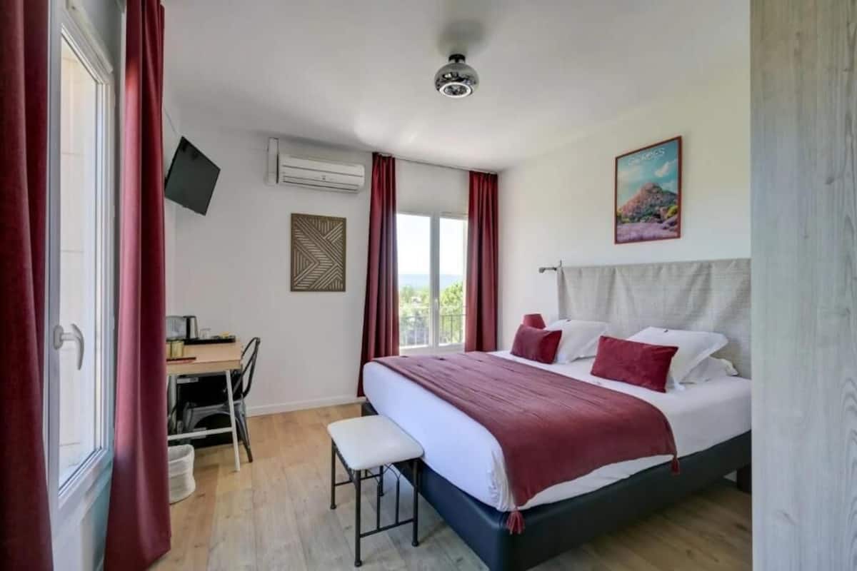 A bedroom with a bed, a desk, a chair, a window with curtains, and a ceiling fan.