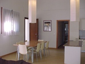 Ein Essbereich mit Holztisch und Stühlen, eine Küche mit weißen Schränken und eine Tür zu einem anderen Raum.