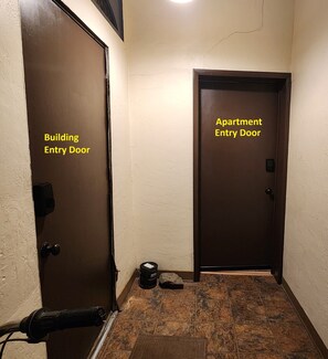 Eine Gebäudetür und eine Wohnungstür mit strukturierter Wand und Fliesenboden.